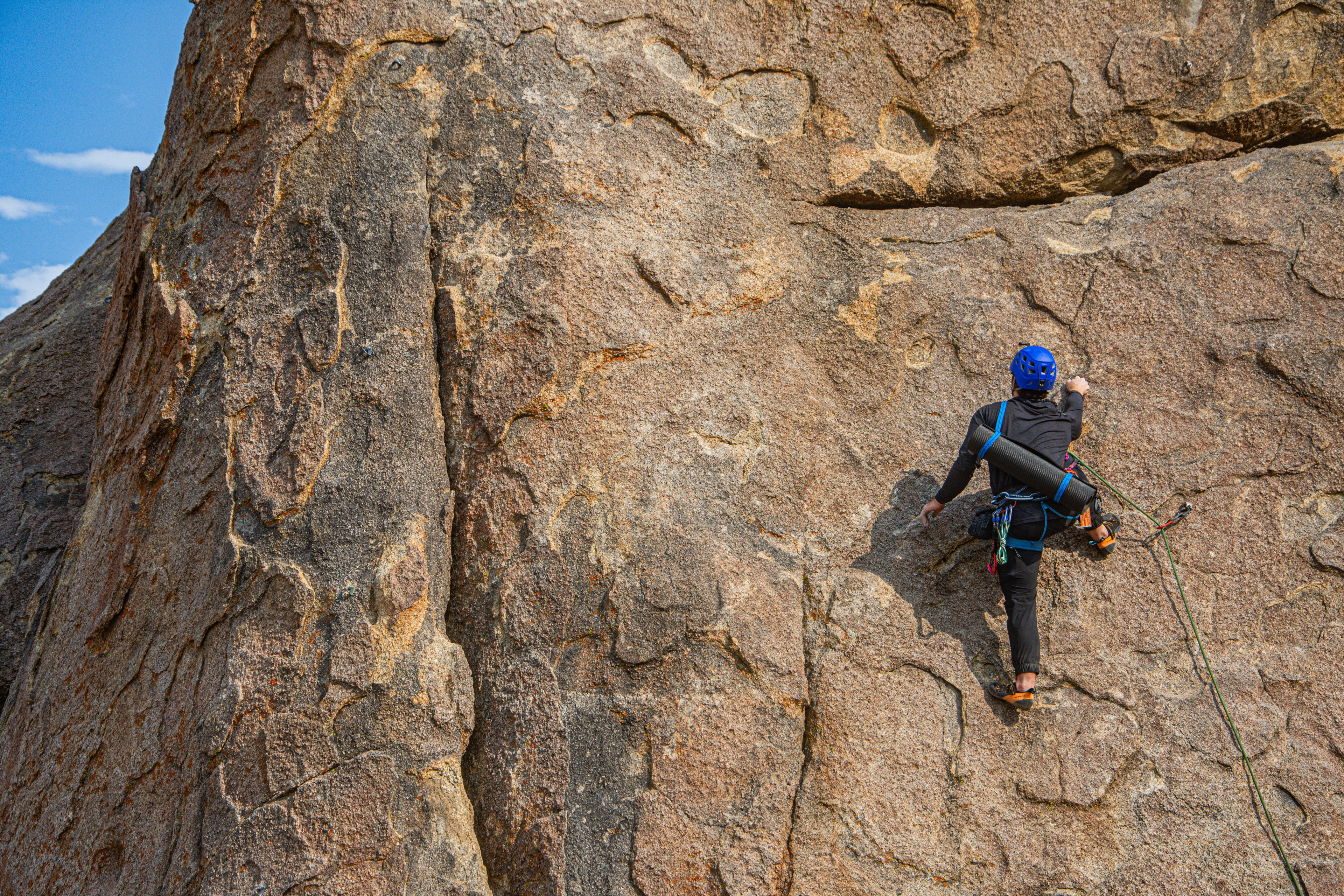 Person climbing a rocky cliff face carrying a yoga mat strap - adventure yoga mat strap