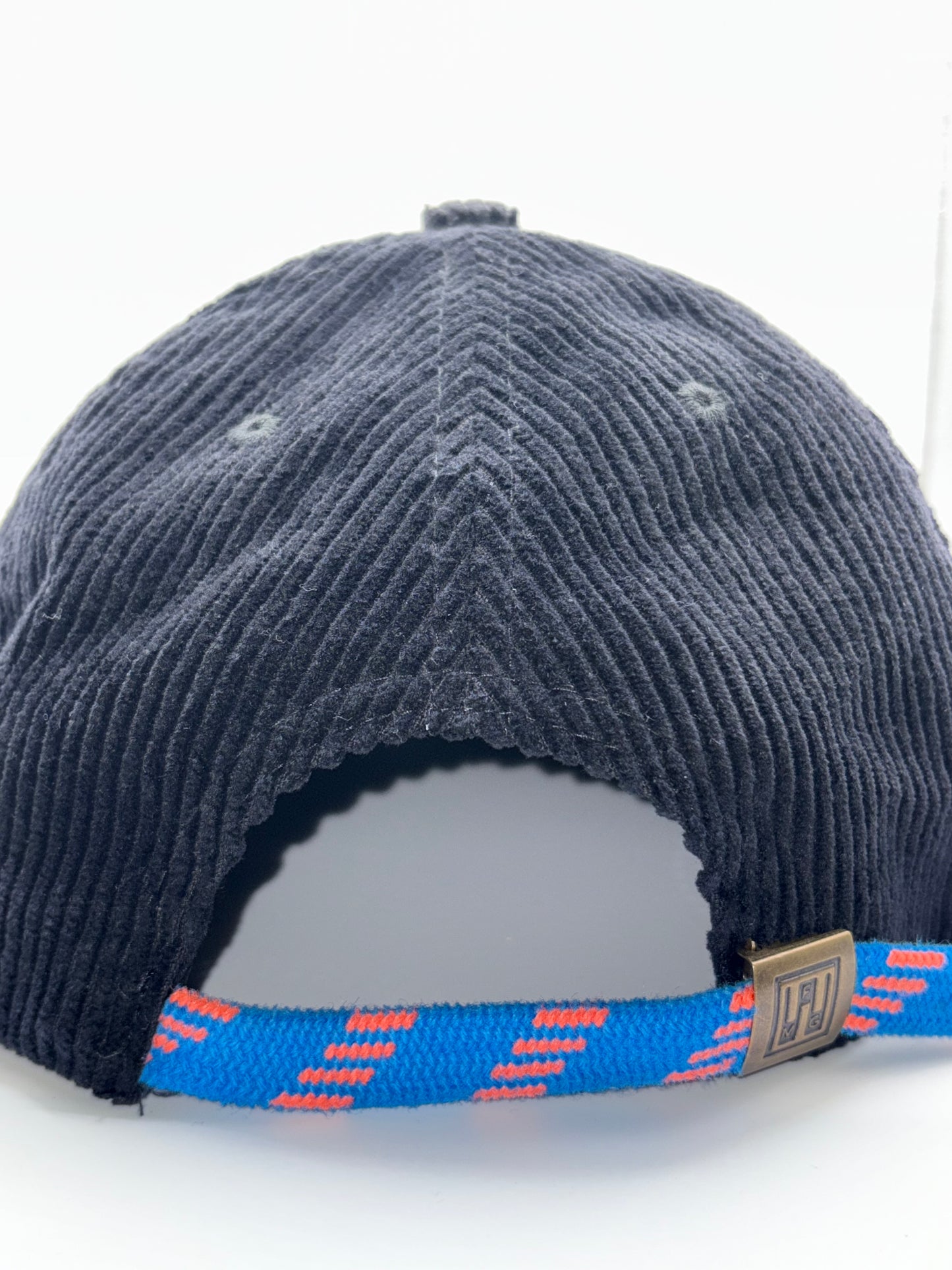 Navy blue cap with a blue strap featuring red patterns on a white background