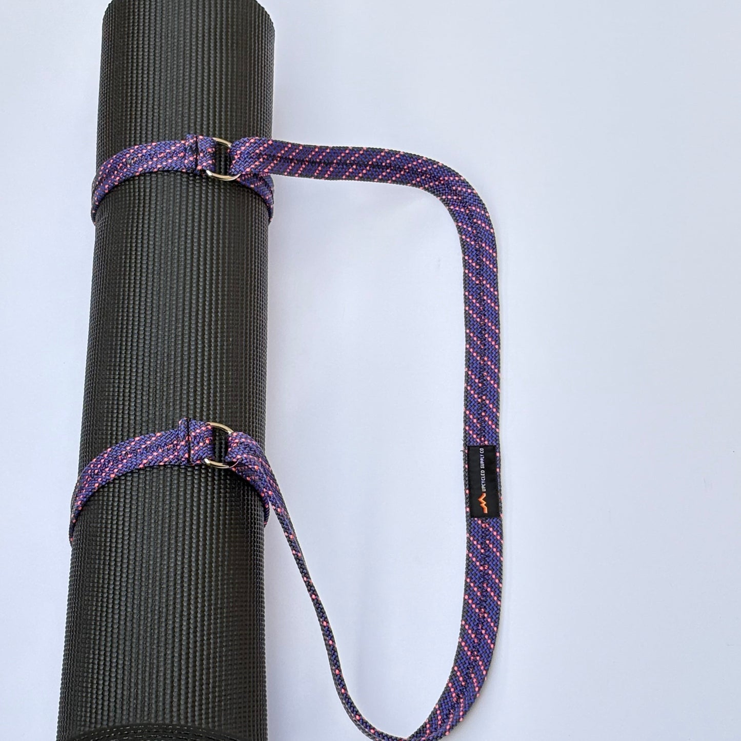 Black yoga mat with a purple strap on a white background