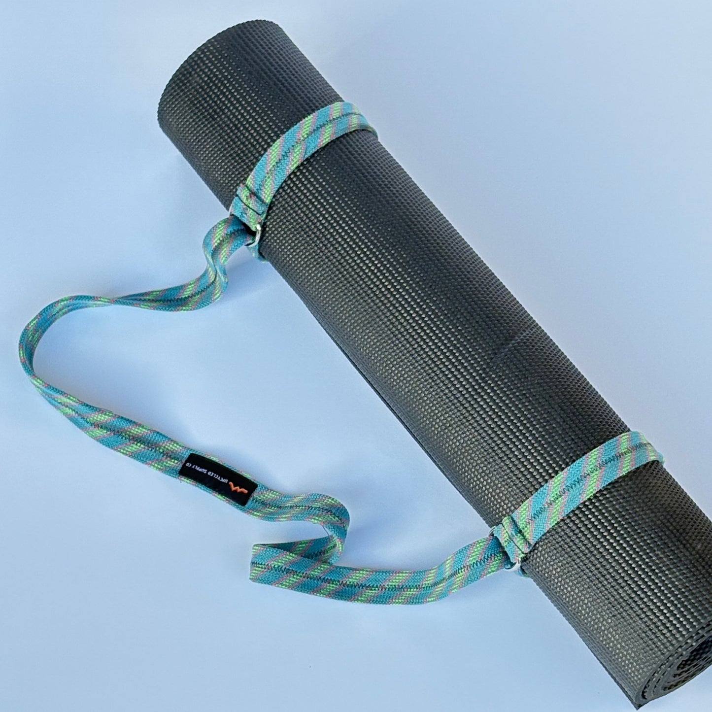 Black yoga mat with a green and blue strap on a light blue background
