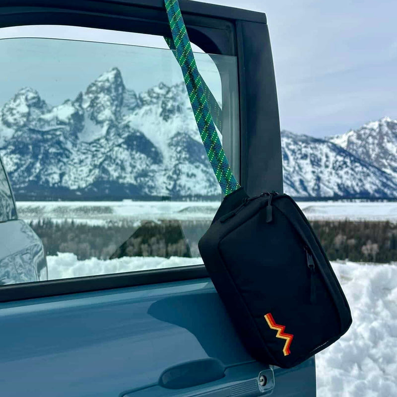 Black bag with a logo attached to a car door against a snowy mountain landscape