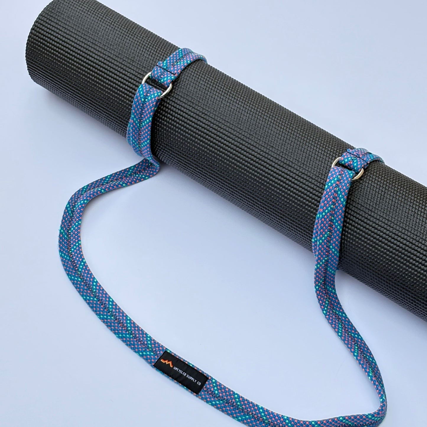 Black yoga mat with a blue and purple strap on a light gray background