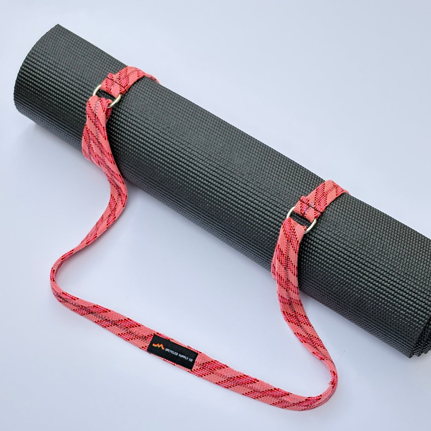 Gray yoga mat with a red carrying strap on a light gray background