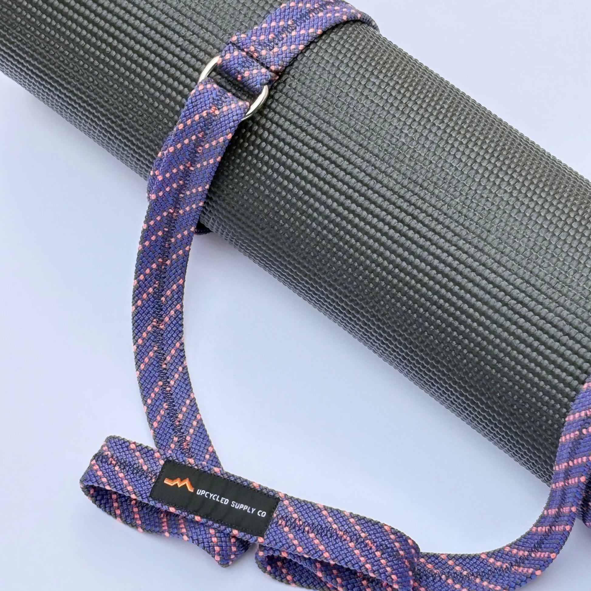 Yoga mat with a purple and blue strap on a light gray background