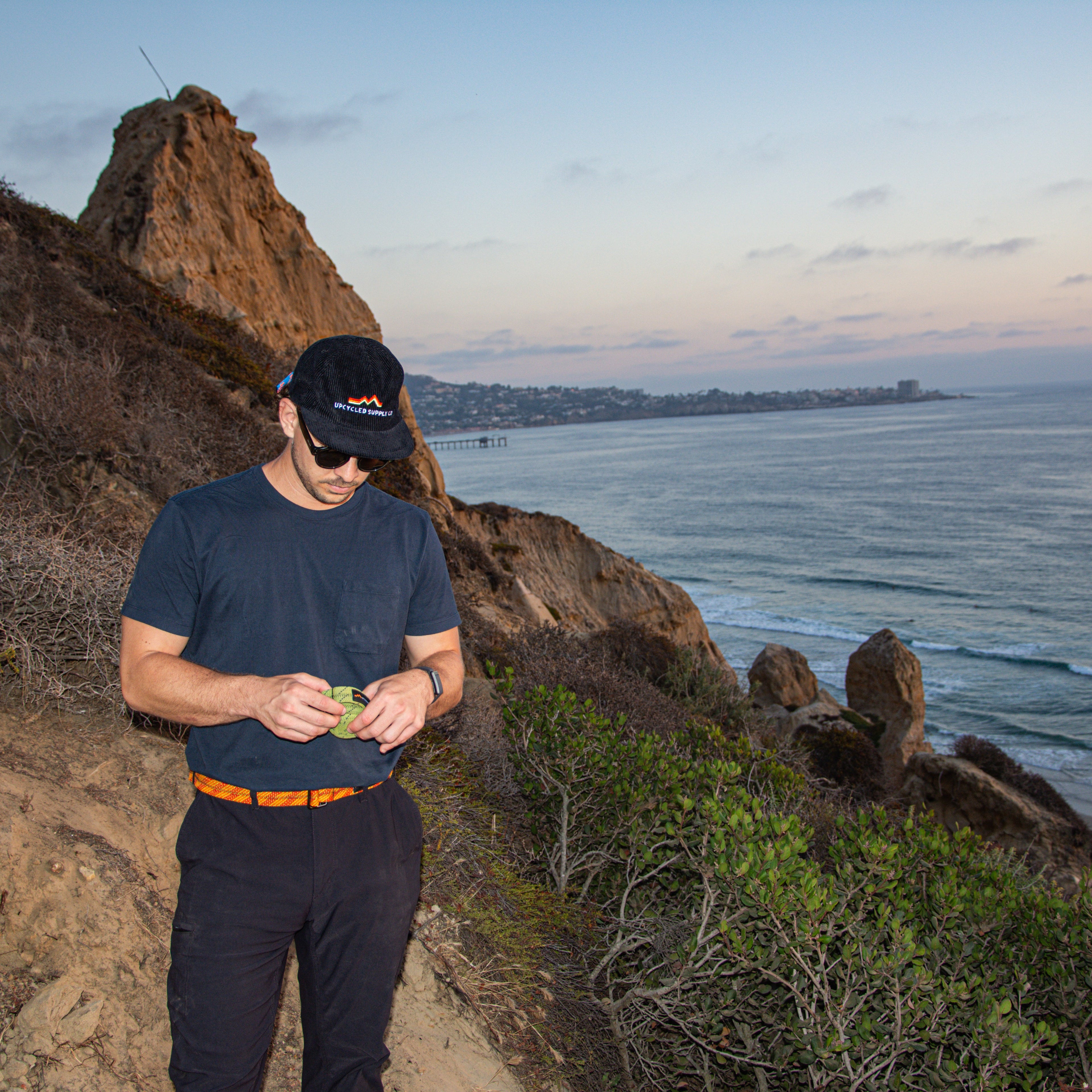 Man standing on a cliff overlooking the ocean at sunset