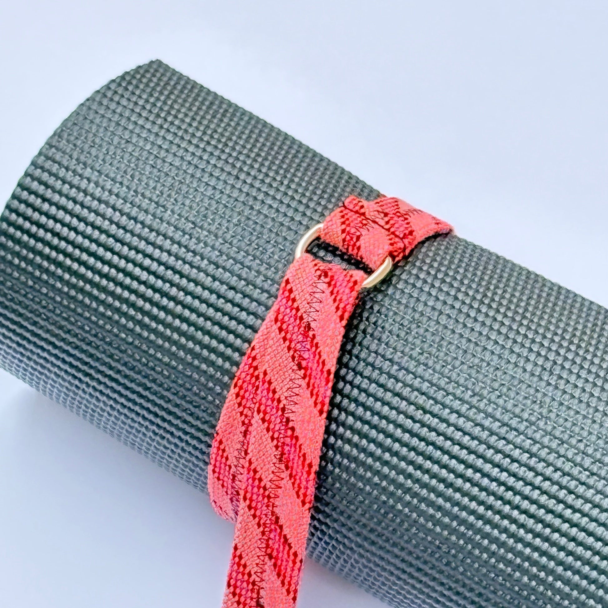 Gray yoga mat with a red strap on a light gray background