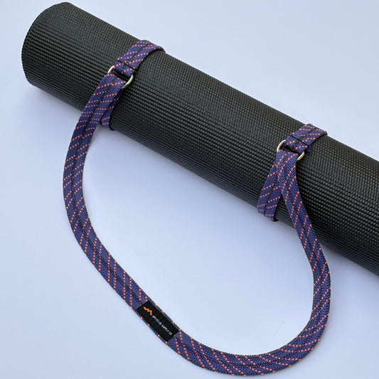 Black yoga mat with a purple strap on a light blue background
