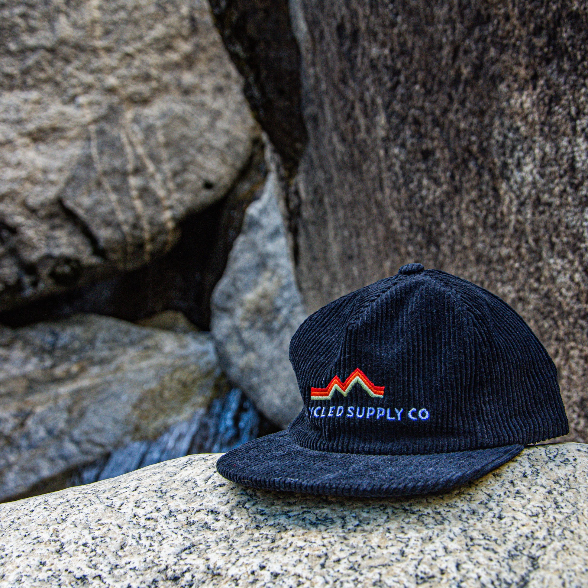 Black cap with a logo on a rock with water and rocks in the background