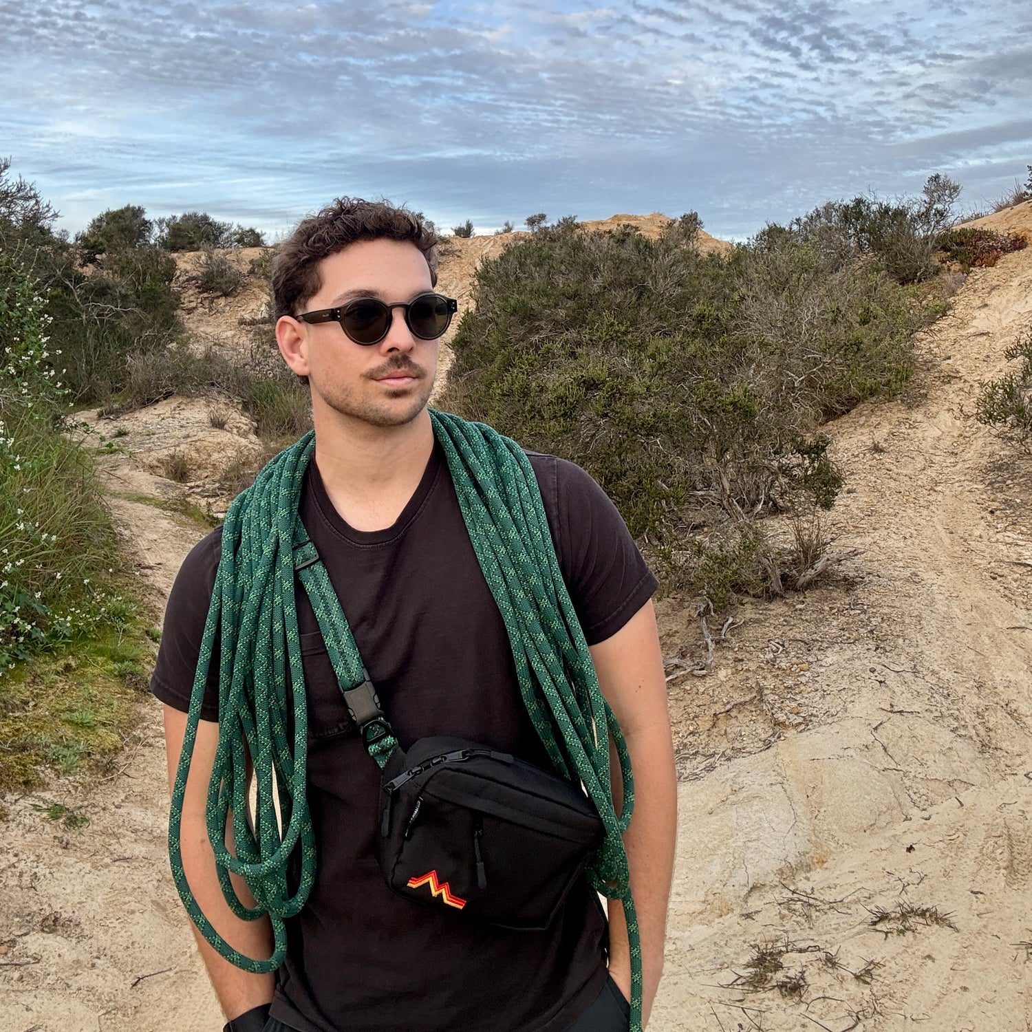 Man standing outdoors with a rope around his neck, wearing sunglasses and a black t-shirt.