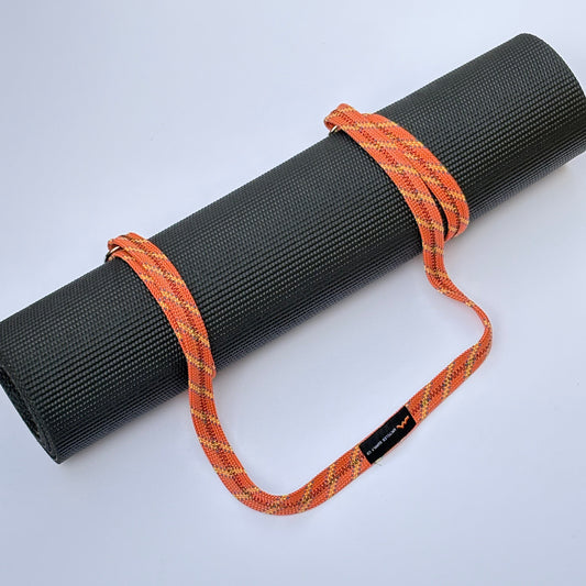Black yoga mat with an orange strap on a light gray background
