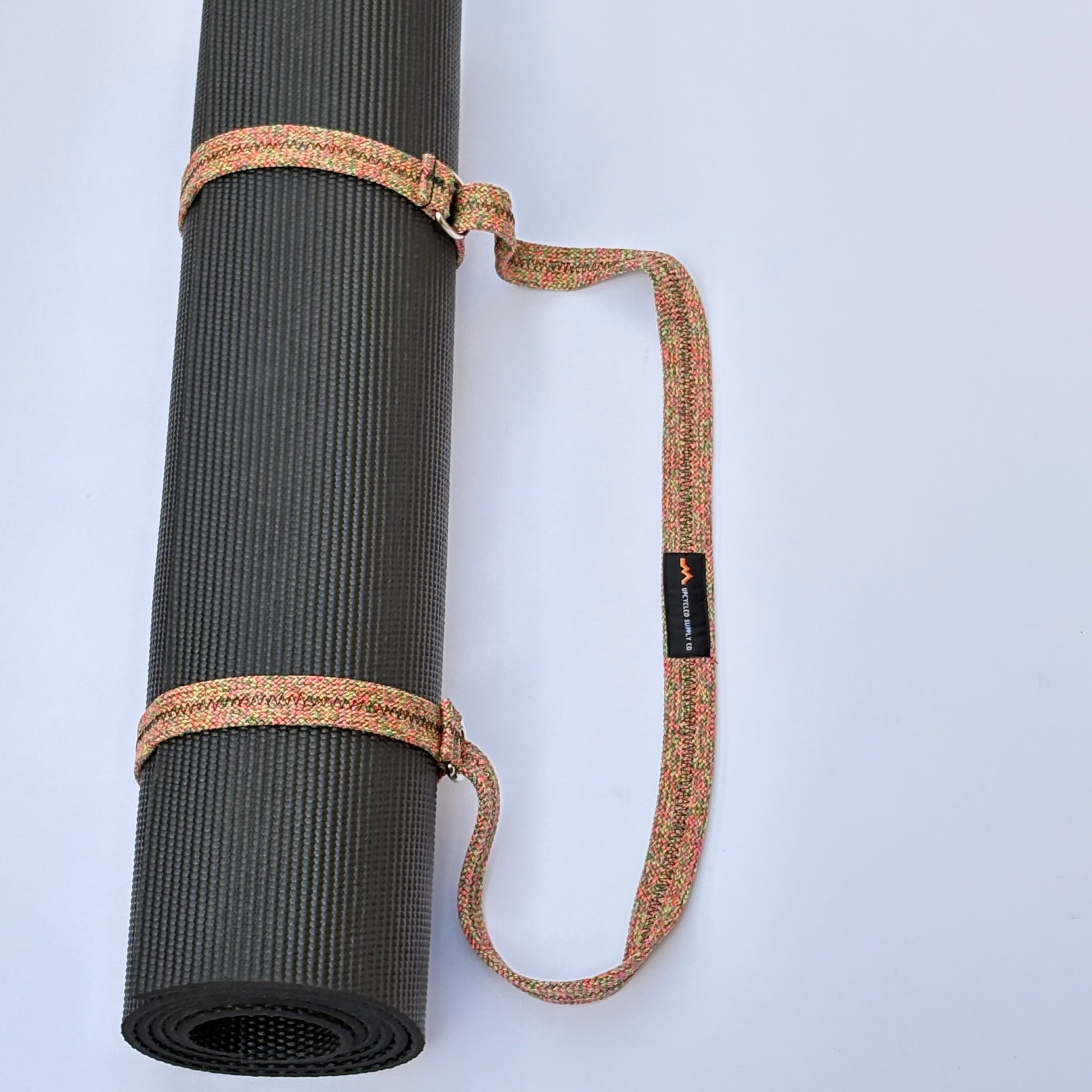 Black yoga mat with a brown carrying strap on a light gray background