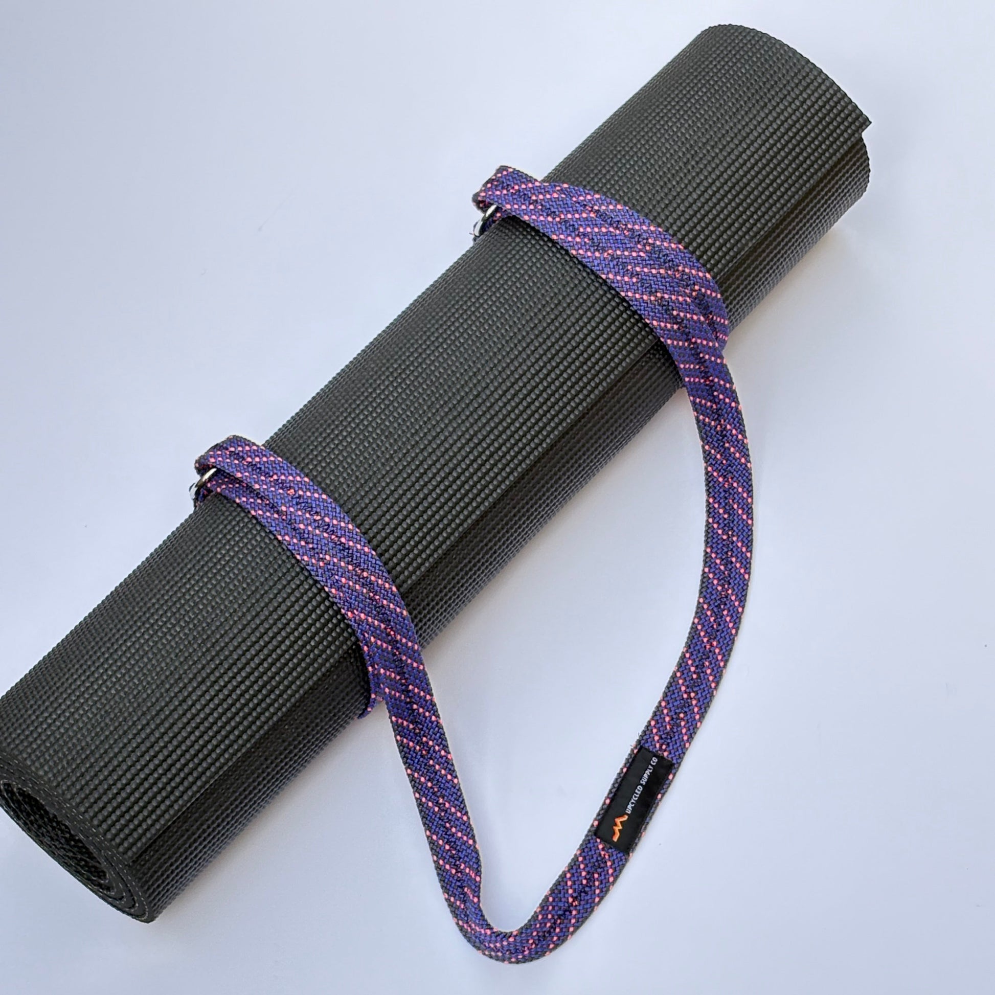Roll of black yoga mat with purple strap on a white background