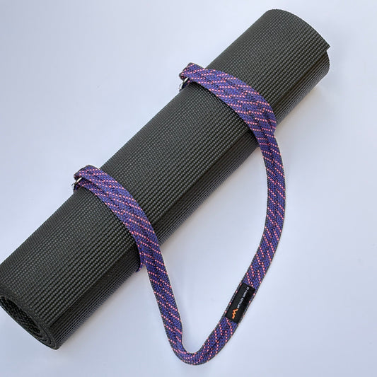 Roll of black yoga mat with purple strap on a white background