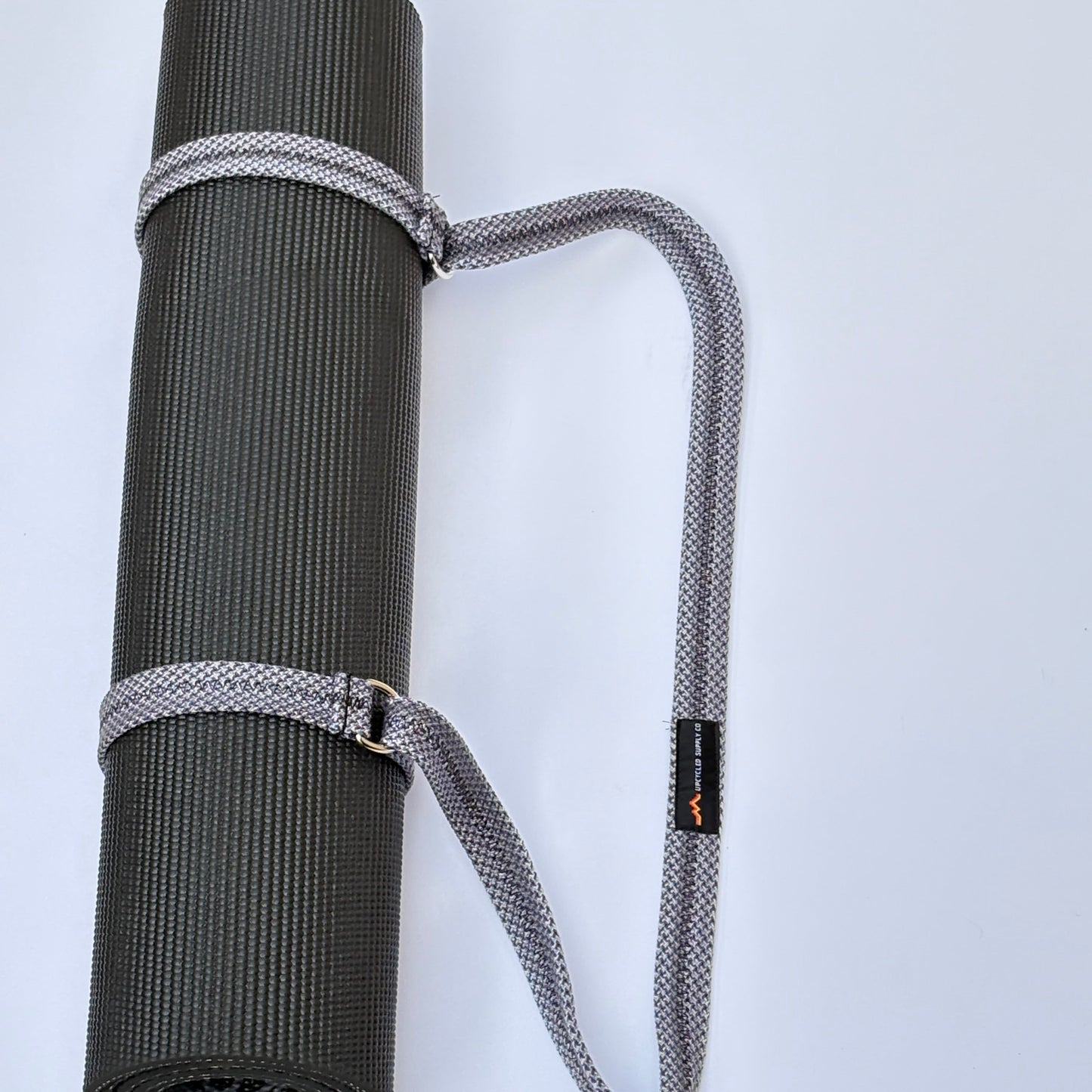 Gray yoga mat with a carrying strap on a light gray background