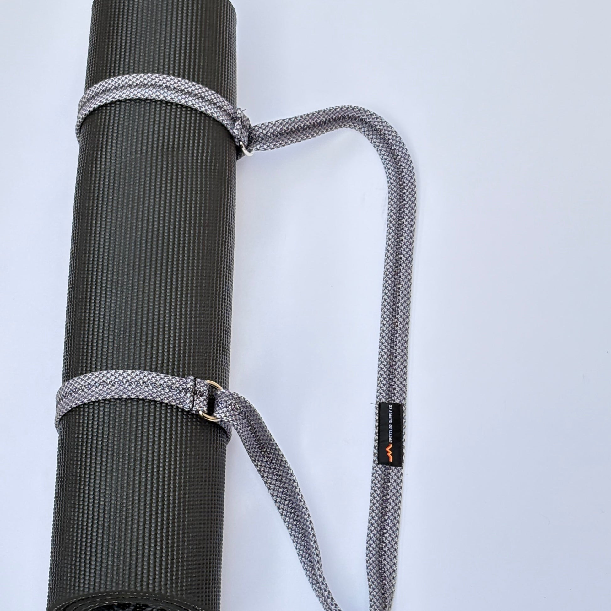 Gray yoga mat with a carrying strap on a light gray background