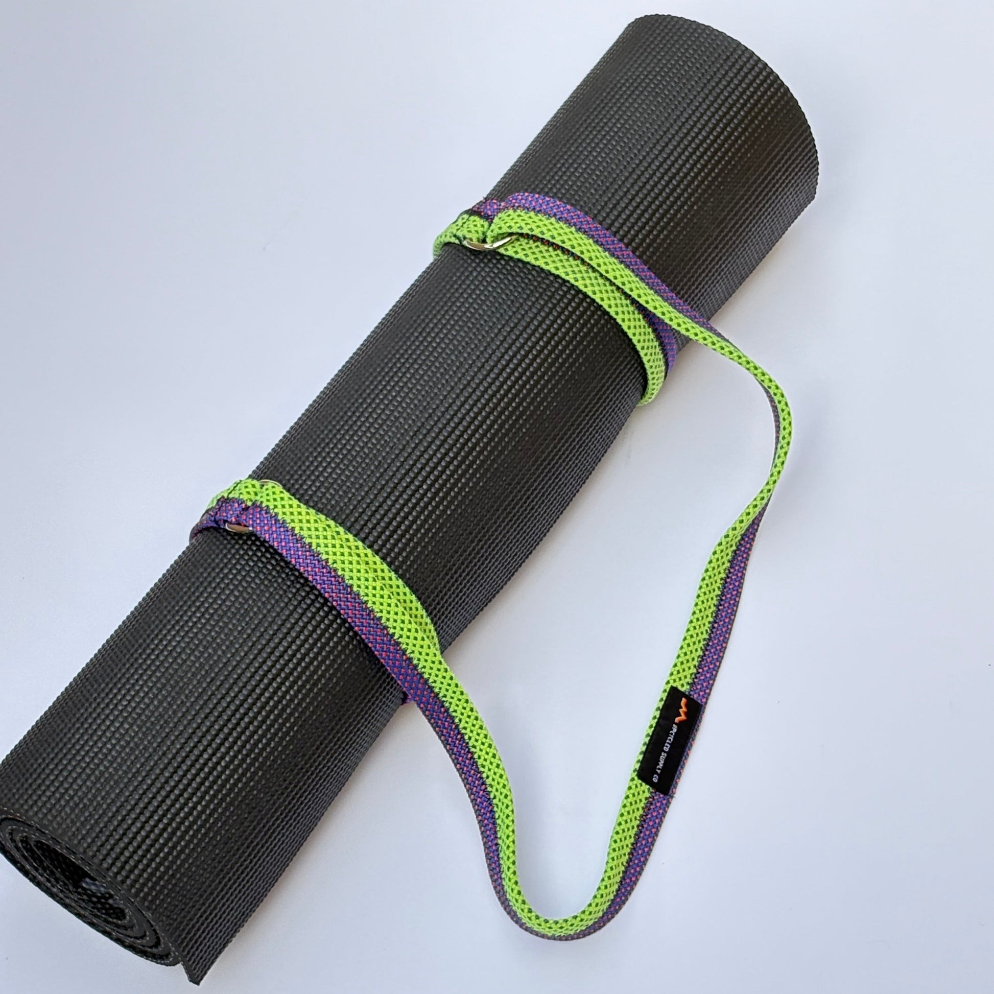 Black yoga mat with a green and purple strap on a white background