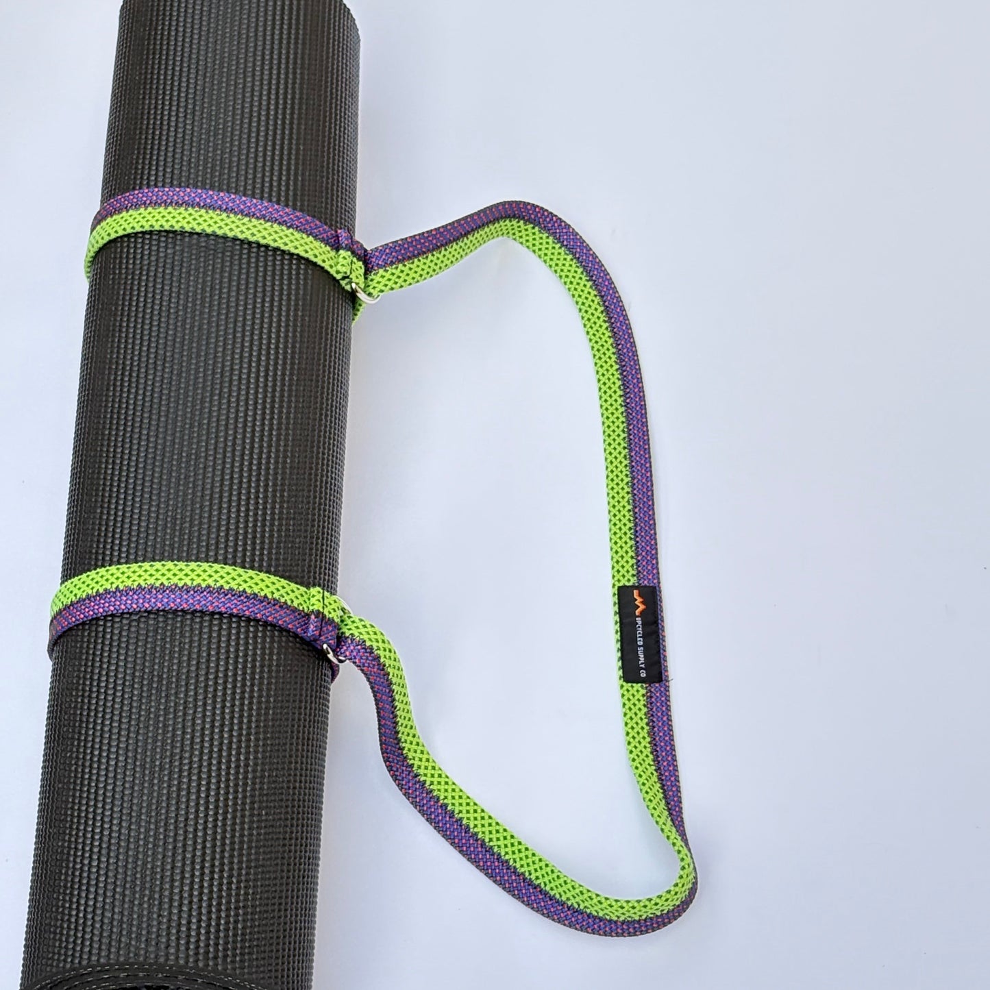 Rolling yoga mat with a purple and green strap on a light gray background