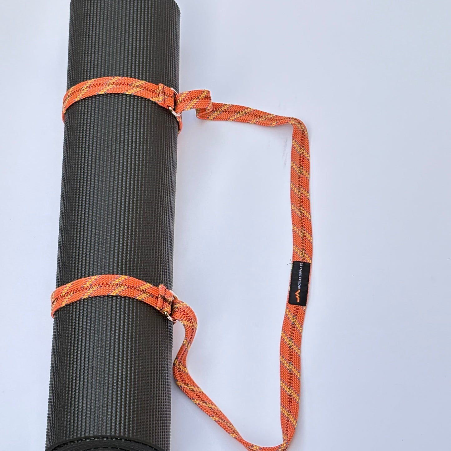 Black yoga mat with an orange carrying strap on a light gray background