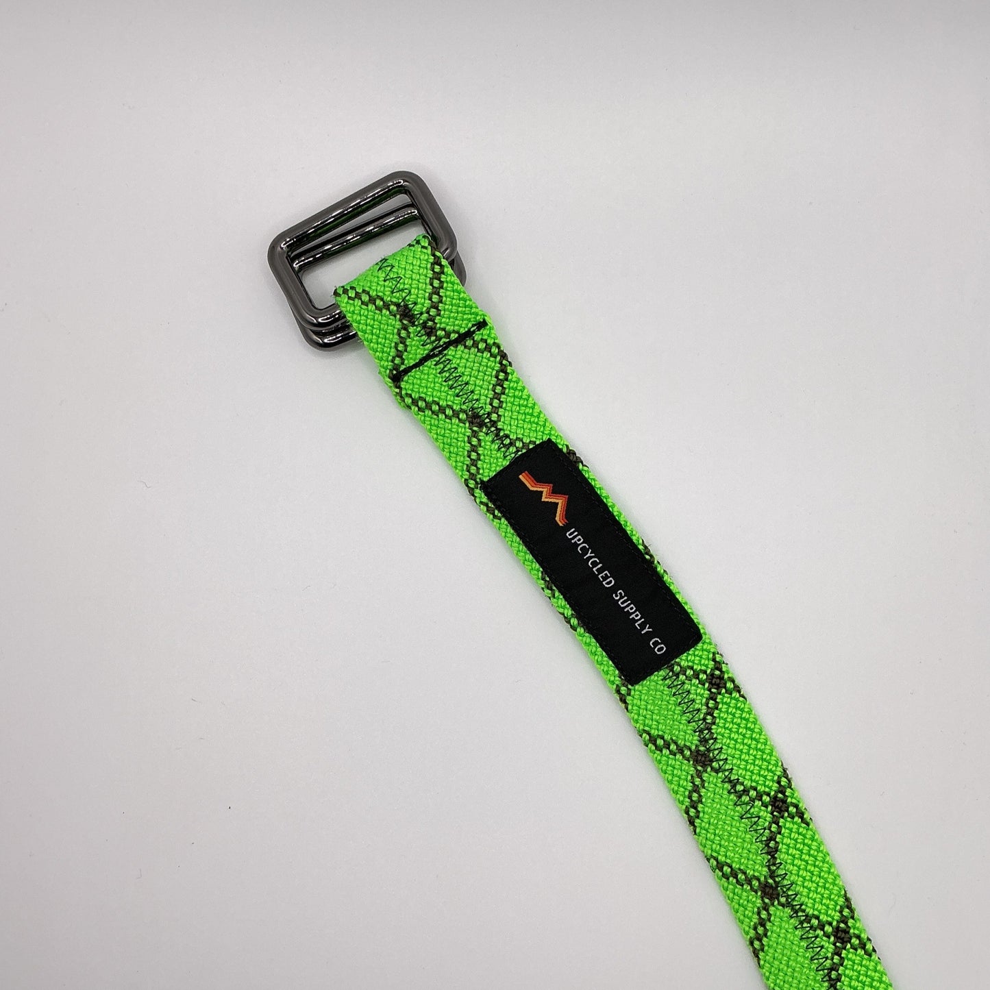 Green webbing strap with a black buckle on a gray background