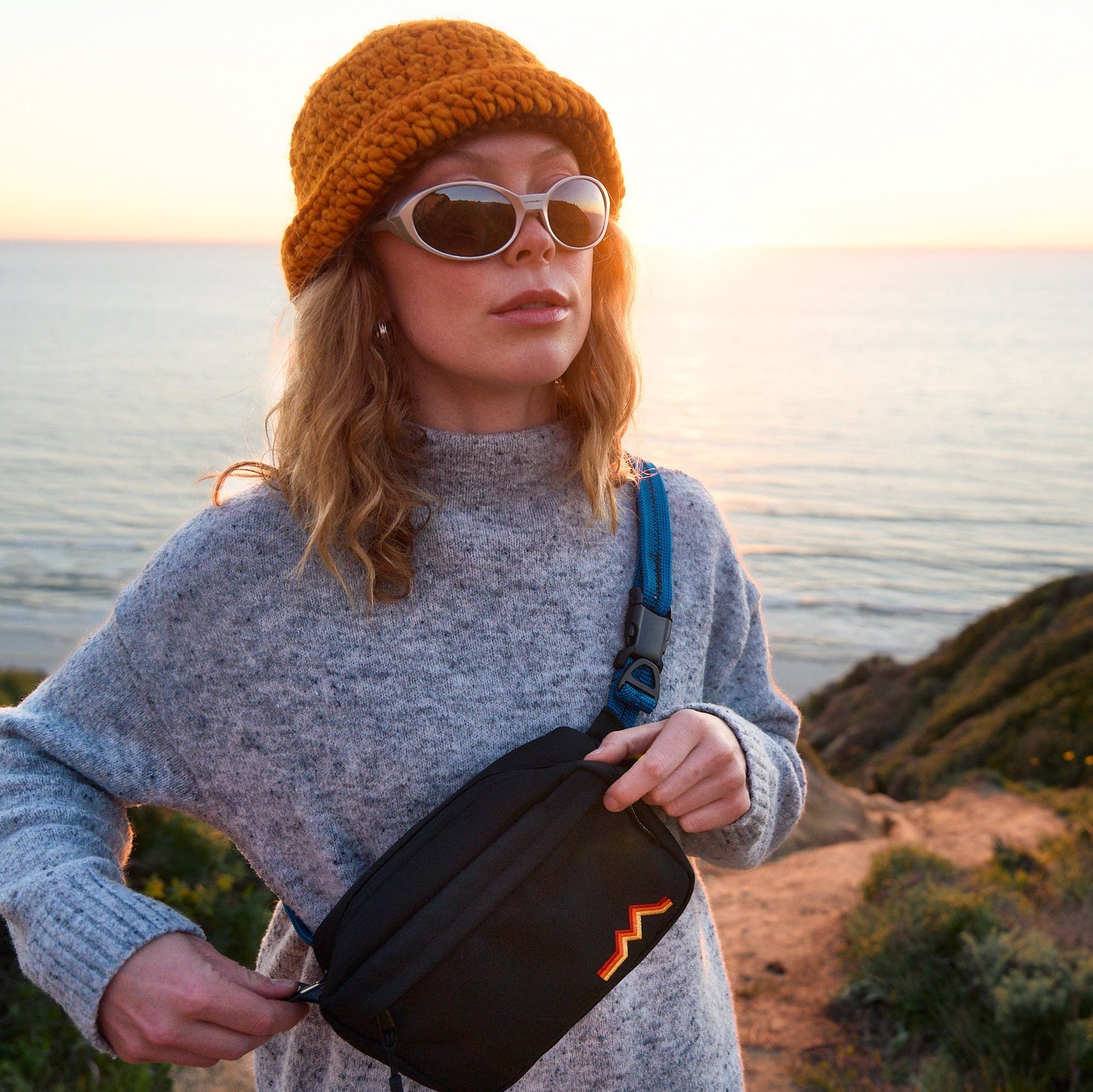 Person holding a black bag with a sunset over water in the background