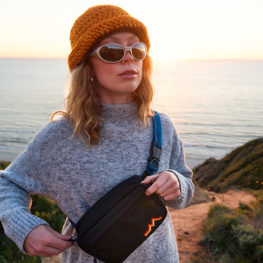 Person holding a black bag with a sunset over water in the background