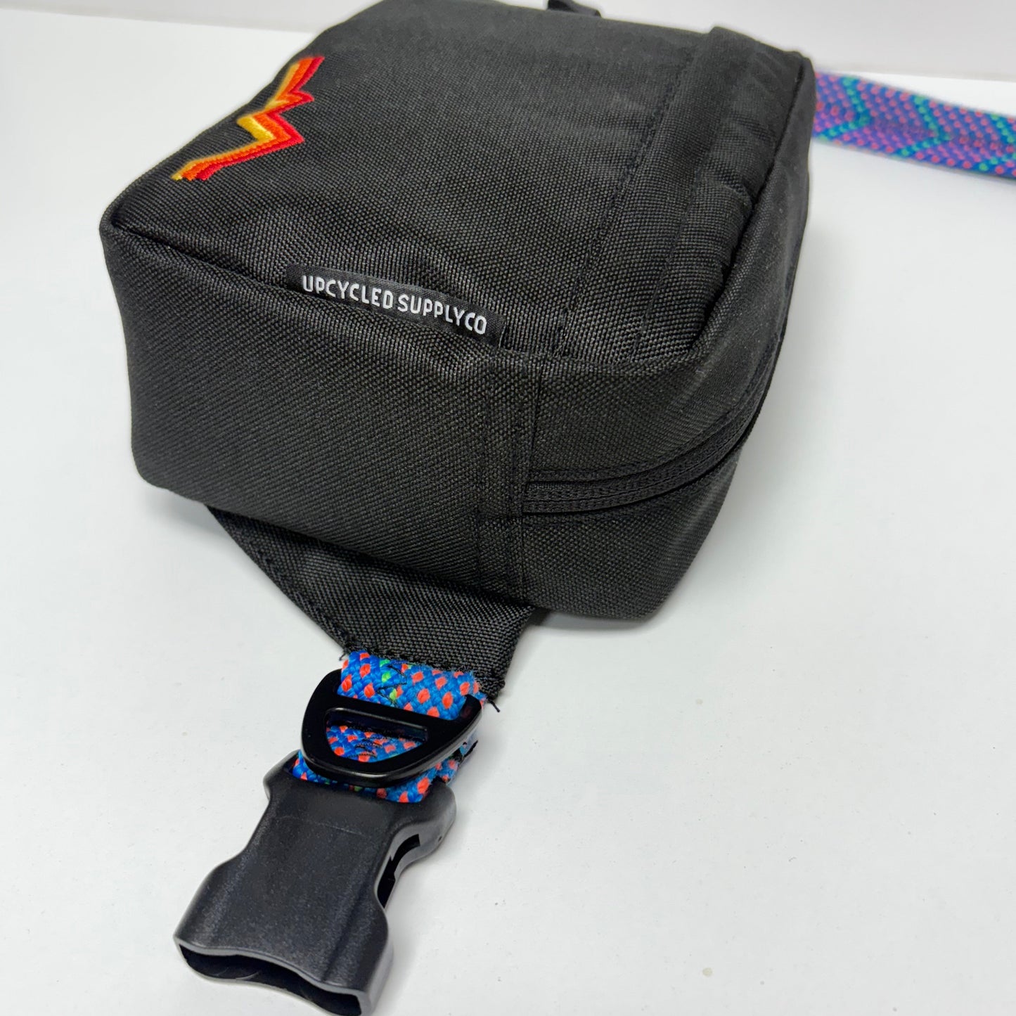 Black sling bag with colorful strap on a white background