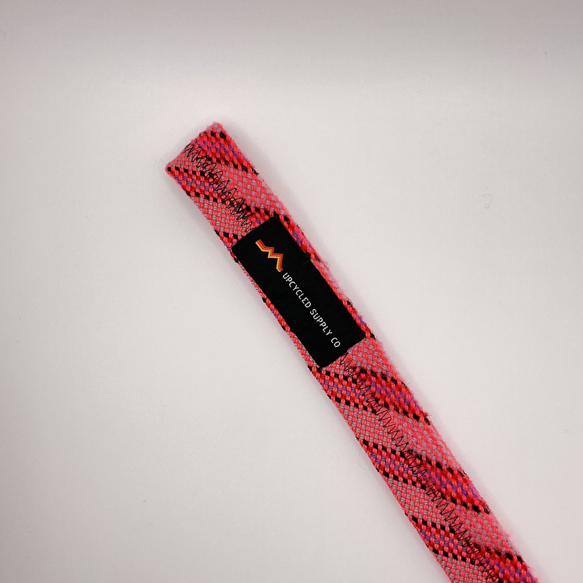 Pink and black patterned belt with a visible brand label on a light gray background