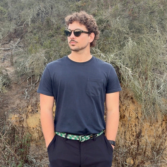 Man wearing sunglasses and a dark shirt standing in a natural setting with trees and rocks.